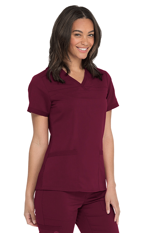 A woman wearing a red Dickies scrub top with a V-neckline and short sleeves, paired with matching red scrub pants.